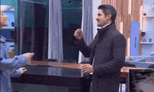 a man and a woman are standing next to each other in a kitchen and talking to each other .