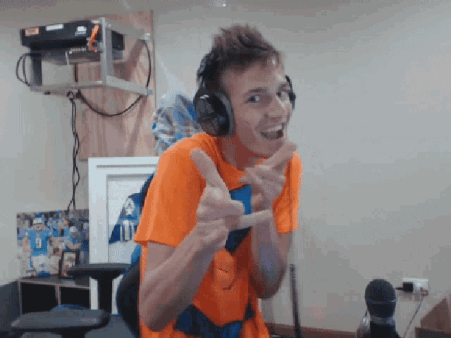 a man wearing headphones and an orange shirt giving the thumbs up