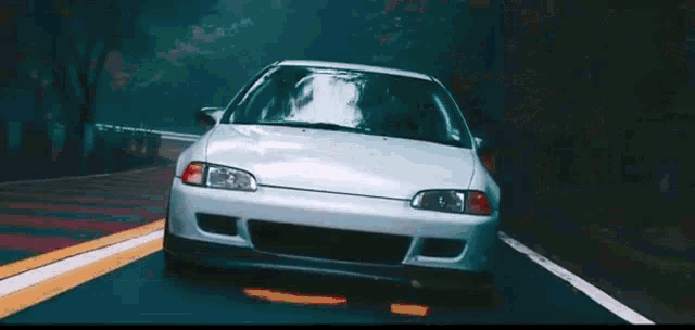 a white car is driving down a road .