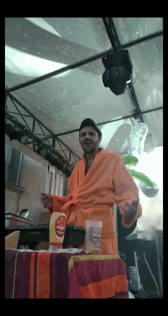 a man in an orange robe is standing in front of a table with a bottle of heinz mustard