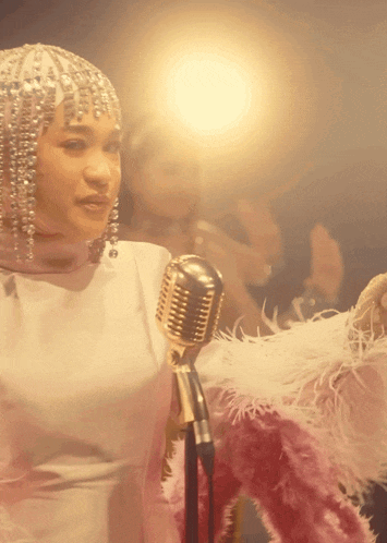 a woman is singing into a microphone while wearing a feathered outfit