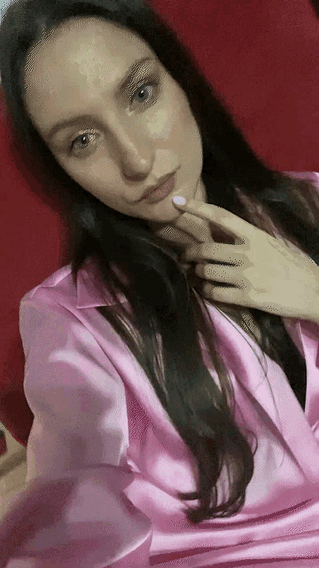 a woman wearing a pink satin shirt is taking a selfie