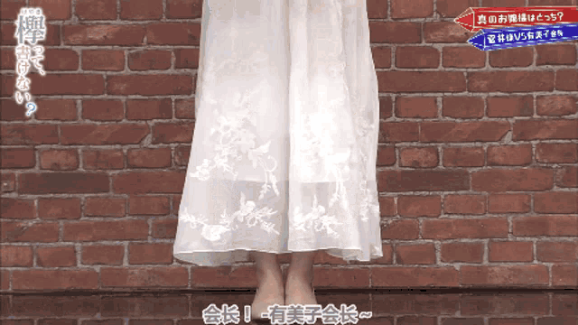 a woman in a white dress stands in front of a red brick wall