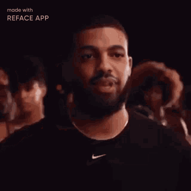 a man with a beard wearing a black nike shirt is standing in front of a crowd of people .