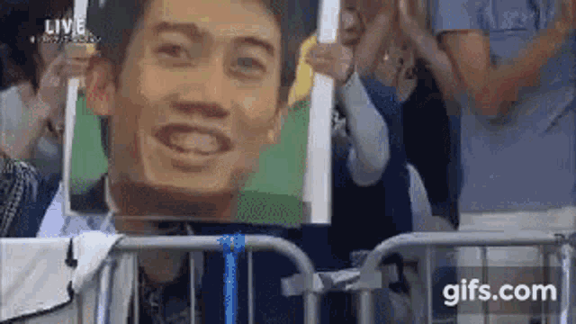 a man is holding a picture of a man 's face in front of a crowd of people .