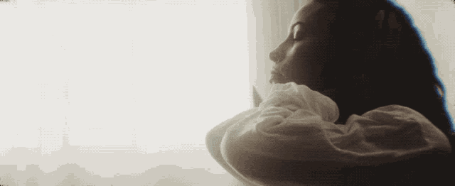 a woman in a white shirt looks out a window