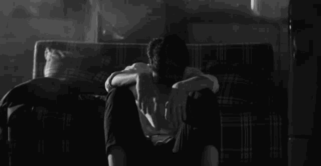 a black and white photo of a man sitting on a couch with his head in his hands .