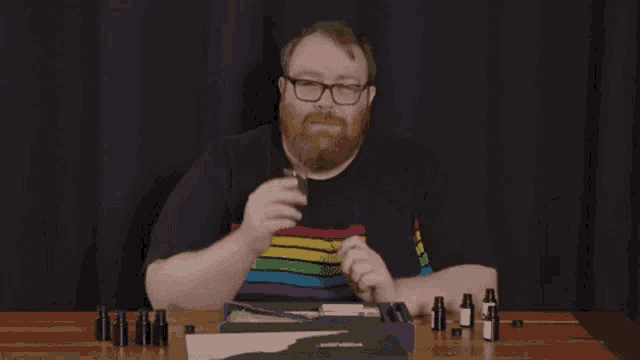 a man wearing glasses and a rainbow shirt covering his mouth