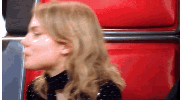 a woman with blonde hair is sitting in a red chair with her eyes closed