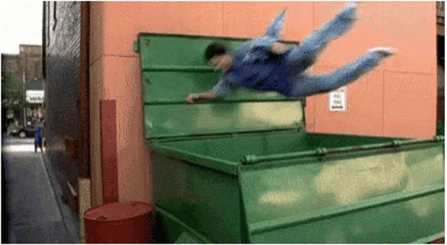 a man is jumping into a green dumpster with a sign that says no dogs