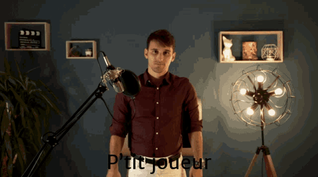 a man in a red shirt stands in front of a microphone with the words p'tit joueur above him