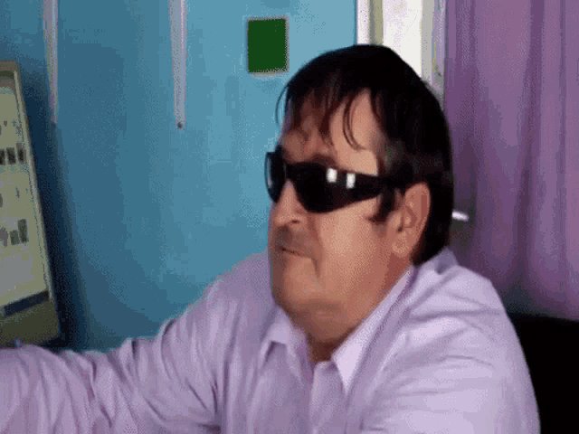 a man wearing sunglasses and a purple shirt is sitting in front of a computer .