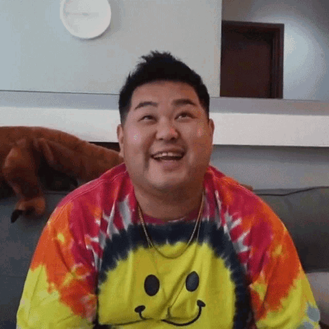 a man wearing a tie dye shirt with a smiley face on it smiles