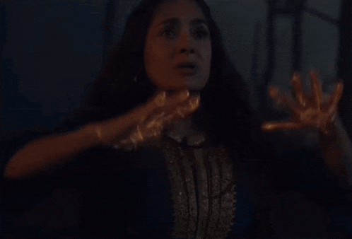 a woman in a blue and gold dress is holding her hands out in the dark .