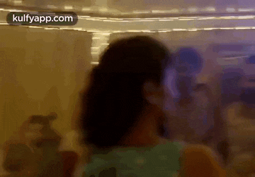 a woman in a blue shirt is dancing in a room with a crowd of people .