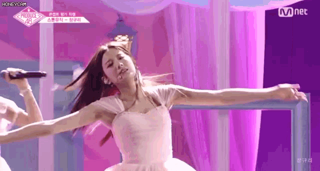 a woman in a pink dress is dancing on a stage with her arms outstretched while holding a microphone .