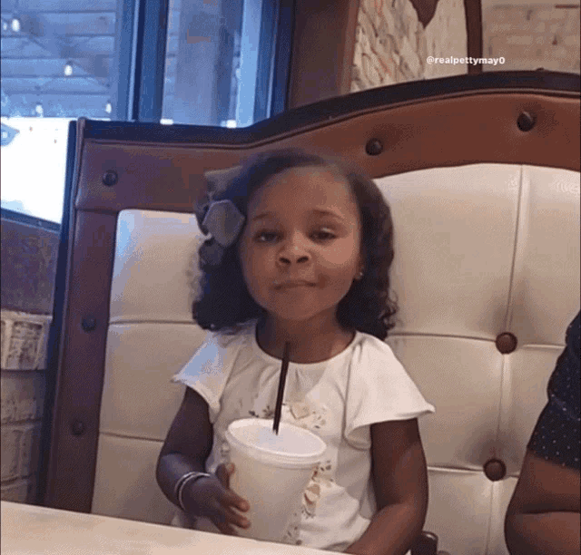 a little girl sitting in a chair holding a cup with a straw in it