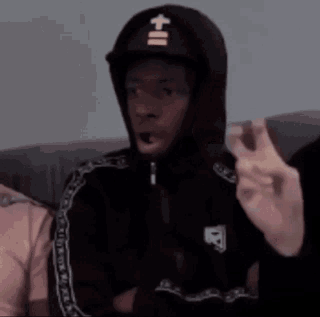 a man in a hoodie and hat is sitting on a couch .