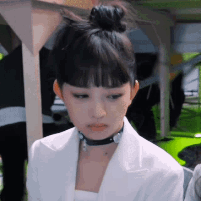 a woman wearing a white jacket and a black choker looks at the camera .