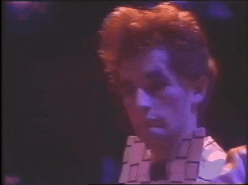 a close up of a man 's face in a dark room with purple lights behind him .