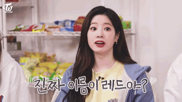 a girl in a yellow shirt and a blue jacket is making a funny face in front of a shelf full of snacks