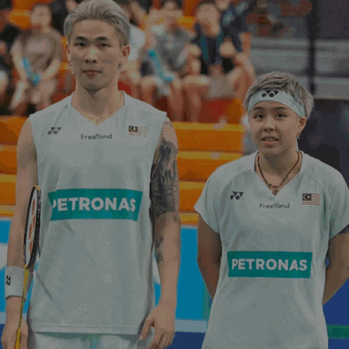 a man and a woman are standing next to each other wearing petronas jerseys