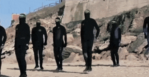 a group of men in wet suits are walking down a beach