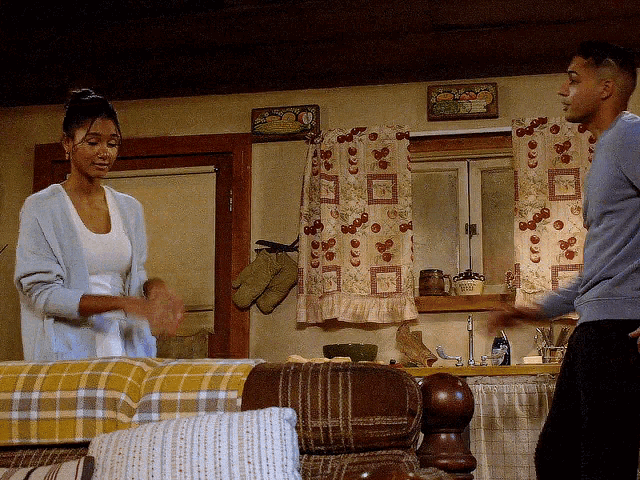 a man and a woman are standing in front of a window with curtains that have a pattern of berries on them