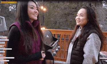 two women are standing in front of a grill and one of them is wearing a vest that says ' nc '