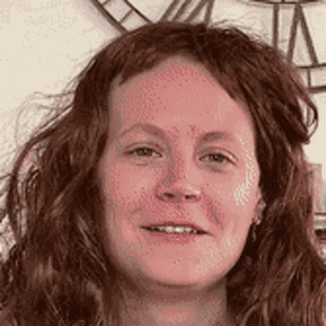 a woman with red hair is smiling in front of a large clock .