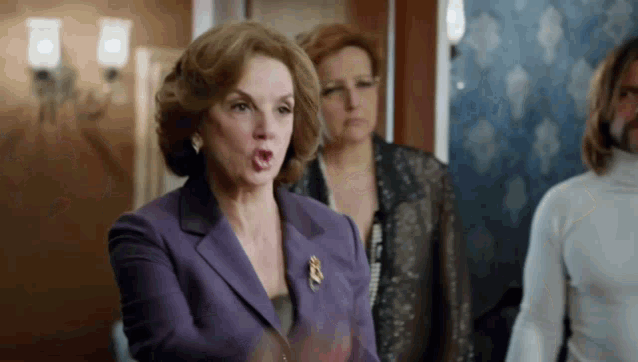 a woman in a purple suit is making a funny face while standing in a room with other women .