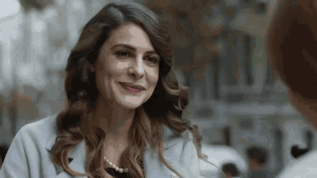 a woman wearing a blue coat and a pearl necklace is smiling .