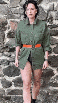 a woman is standing in front of a stone wall wearing a green shirt and orange belt