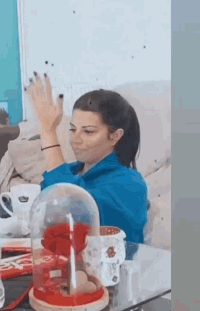 a woman is sitting on a couch with her hands in the air in front of a glass dome with a red rose in it .
