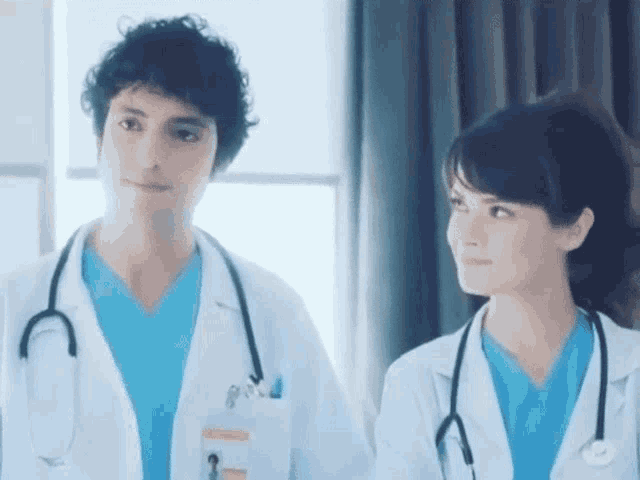 a man and a woman in lab coats with stethoscopes around their necks are standing next to each other .