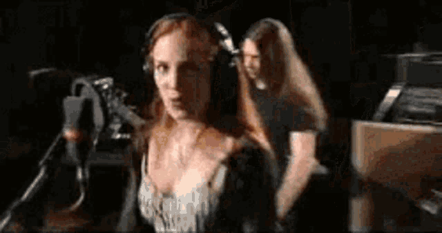 a woman wearing headphones is singing into a microphone while a man stands behind her .