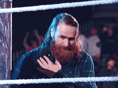 a man with long hair and a beard is standing in a wrestling ring holding a cell phone