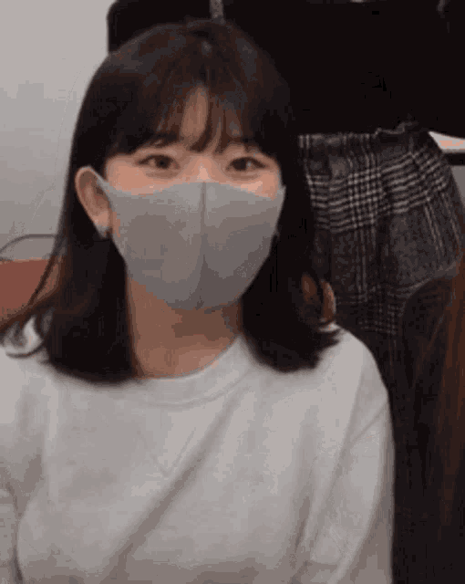 a woman wearing a face mask and a white shirt is sitting in a room .