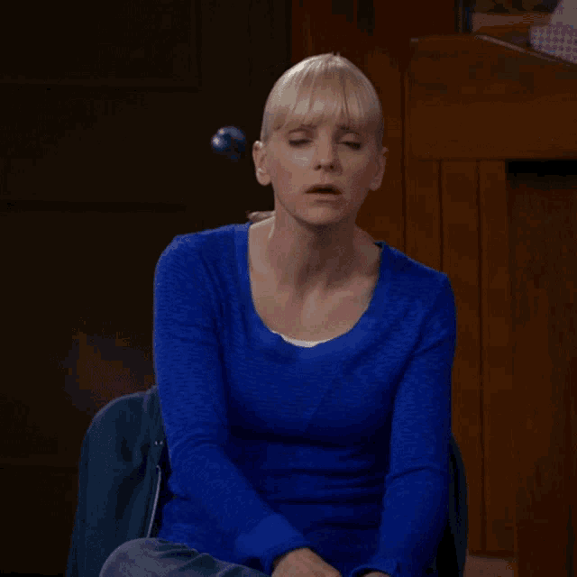 a woman in a blue sweater is sitting in a chair with her mouth open