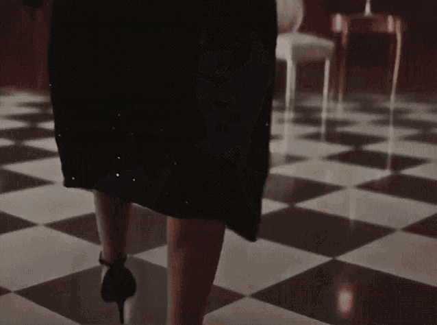a woman in a black dress is walking on a checkered floor in a room .