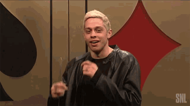 a man in a leather jacket is holding a pair of scissors in front of a playing card .
