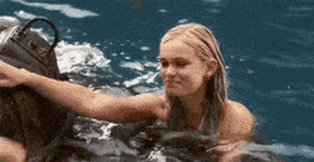 a woman is swimming in the ocean and holding a bag .