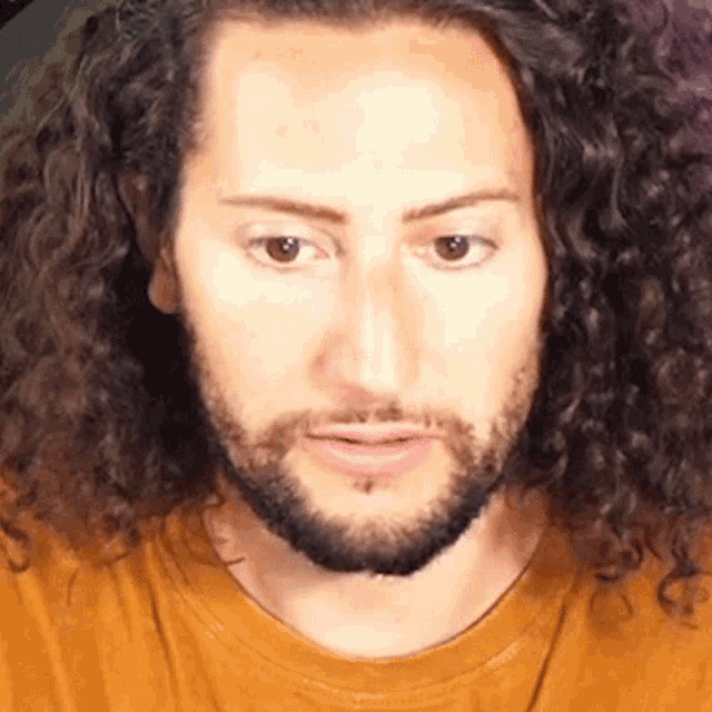 a man with curly hair and a beard is wearing a brown shirt