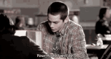 a man in a plaid shirt and tie is sitting at a table talking to another man in a restaurant .