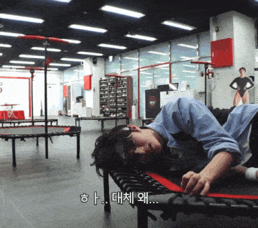 a man laying on a trampoline in a gym with korean writing on the bottom