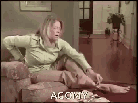 a woman is sitting on a couch in a living room with her legs crossed and a sign that says agomy .