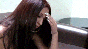 a woman with long nails is sitting in a chair with her hand on her head .