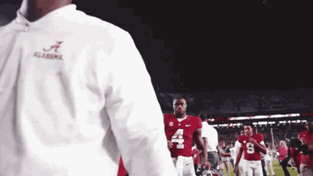 a man wearing a white jacket with the letter a on it stands on a football field
