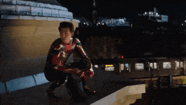 a man in a spiderman suit is kneeling on a ledge