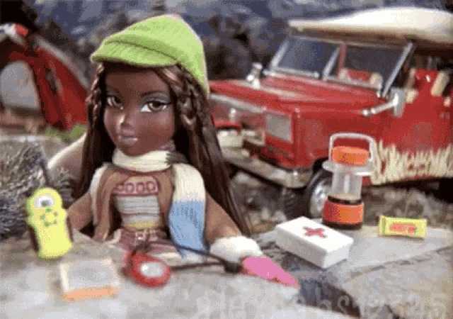 a doll wearing a green hat and scarf is sitting on a rock in front of a red car .